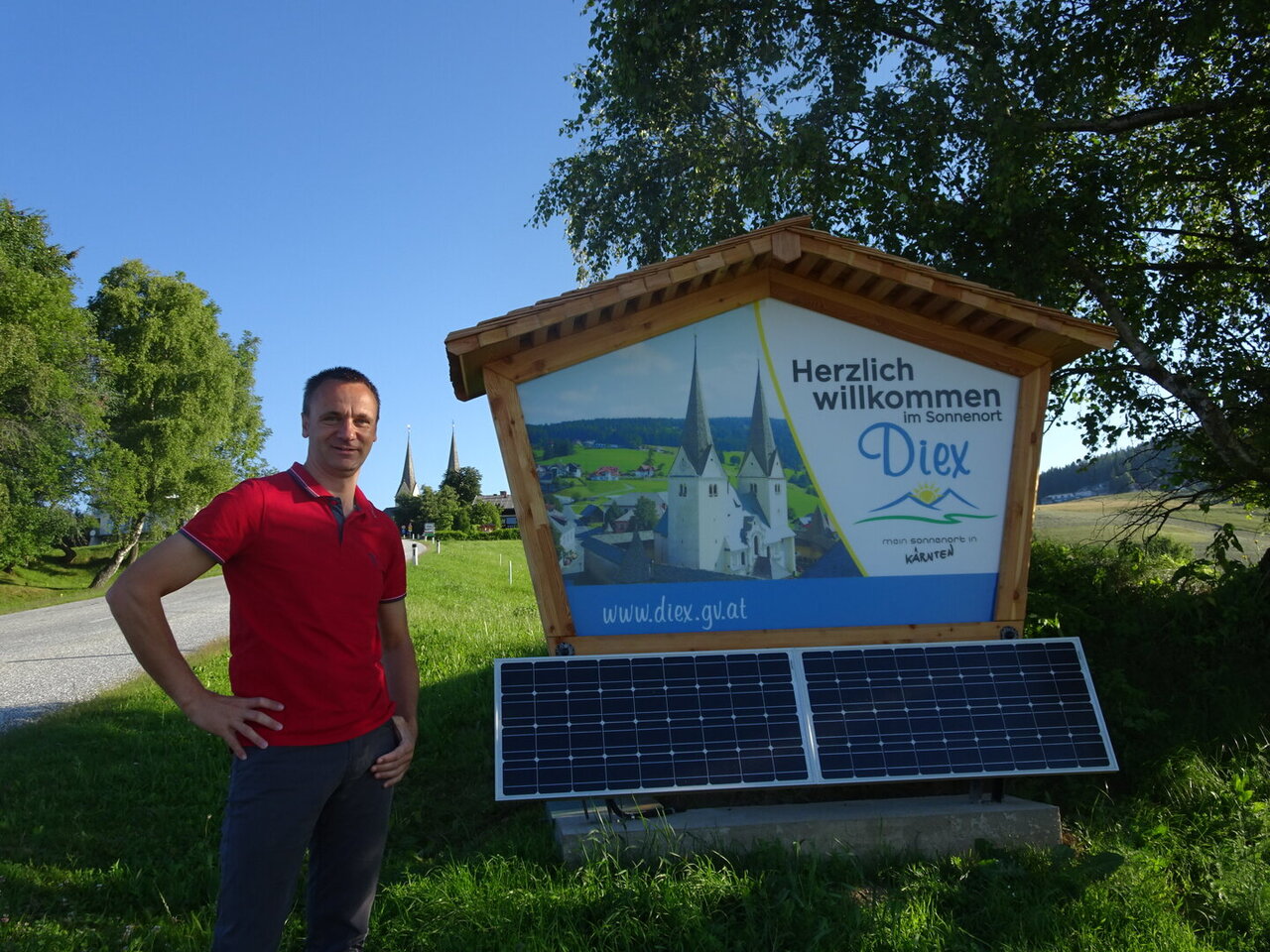 Quelle: Privat Bürgermeister Napetschnig neben Herzlich Willkommen Tafel samt kleiner PV Anlage